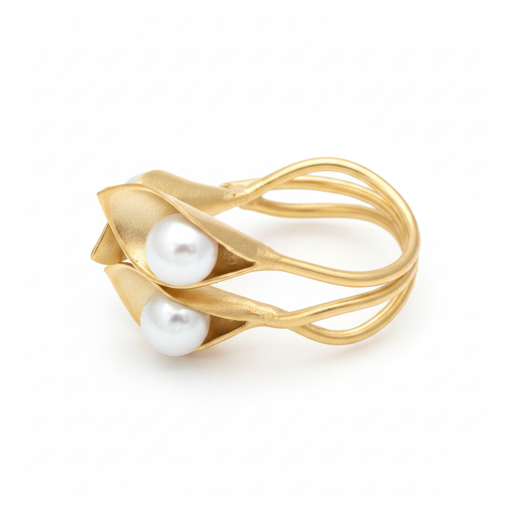 Anillo dorado escultural con dos flores y perlas blancas sobre fondo blanco