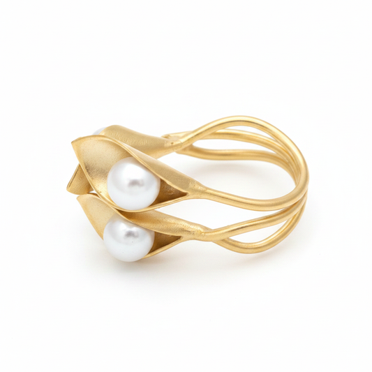 Anillo dorado escultural con dos flores y perlas blancas sobre fondo blanco