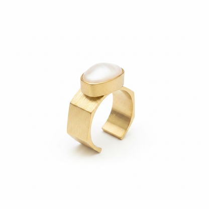 Anillo dorado con textura y piedra ovalada blanca sobre fondo blanco