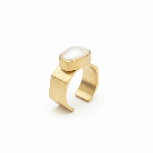 Anillo dorado con textura y piedra ovalada blanca sobre fondo blanco